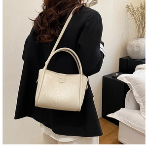 Close-up of cream leather bucket bag with litchi grain and minimalist double handles