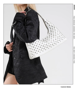 Detailed view of a white leather underarm bag with silver rivets worn by a model