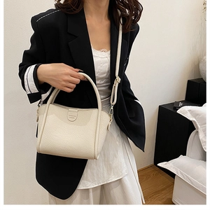 Detailed close-up of cream-colored lychee leather bucket bag with thick top handles