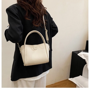 Detail of beige lychee texture bucket bag with dual handles and slim shoulder strap
