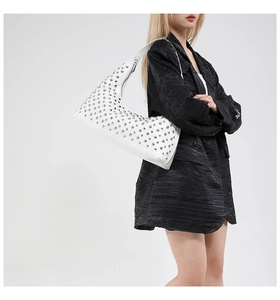 Close-up of white crescent hobo bag with silver studs on a black blazer backdrop