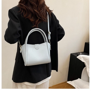 Detail of light blue grain leather bucket bag with top handle and logo on a black blazer