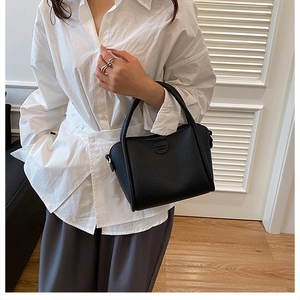 Close-up of black lychee grain leather bucket bag held by a model in a minimalist room