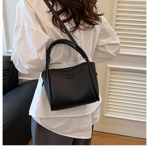 Detail of black pebble leather bucket bag featuring dual handles and adjustable strap