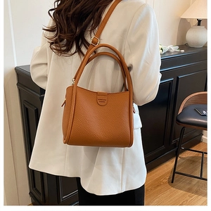 Close-up of caramel brown pebble leather bucket bag with brand logo and slim shoulder strap