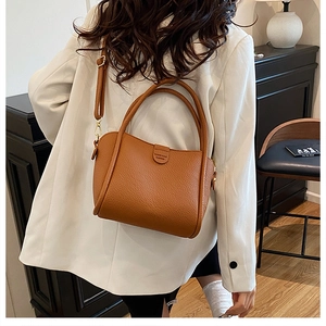 Detail of brown lychee pattern leather bucket bag with top handles and logo strap