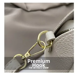 Close-up of golden metal hooks and lychee grain leather strap on a beige bucket bag