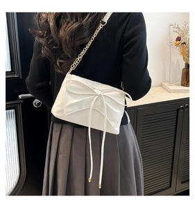 Detailed view of white bow crossbody bag with gold chain strap on model's shoulder