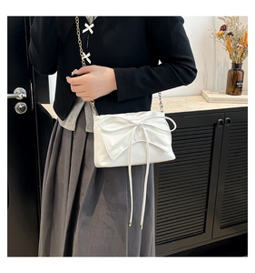 Close-up of white PU leather bag with large bow and gold metal chain strap detail