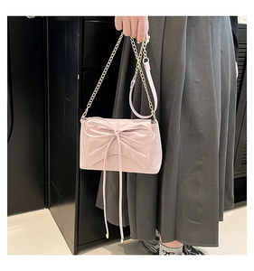 Detail view of the large bow decoration and gold chain strap on the light pink bag