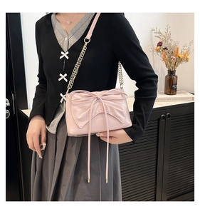 Detail of light pink crossbody bag with large bow and gold metal chain strap