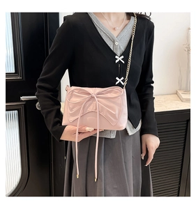 Detail of light pink crossbody bag with 3D bow and elegant gold metal chain strap
