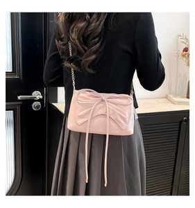 Detail of a sweet pink crossbody bag with a large bow and gold chain strap on model