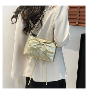 Close-up of metallic light gold shoulder bag with a large bow and elegant chain strap