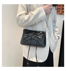 Close-up of black glossy leather bag featuring a large bow and gold metal chain strap