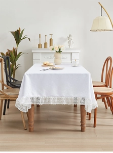 Detail van een elegant wit rechthoekig tafelkleed met verfijnde kanten randen op hout