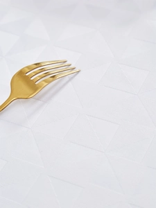Detail van wit waterdicht tafelkleed met geometrische jacquard en een gouden vork