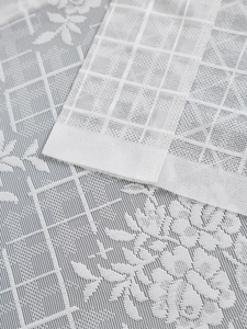 Detail of white French lace curtain with delicate floral patterns and mesh texture