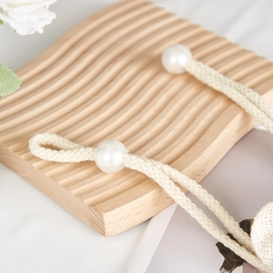 Close-up of cream woven rope curtain tieback with large white pearls on a wooden tray