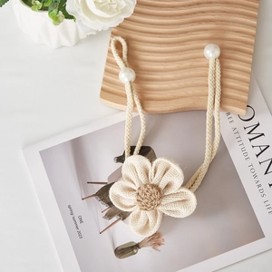 Detail of floral curtain tieback with woven rope and pearl accents on a wooden board