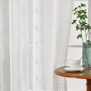 White French lace curtain with floral embroidery hanging in a bright, cozy living room