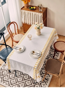 Close-up detail of white rectangular tablecloth with yellow floral embroidery and woven texture