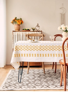 Detail of white cotton linen tablecloth with yellow geometric embroidery and tassel edges