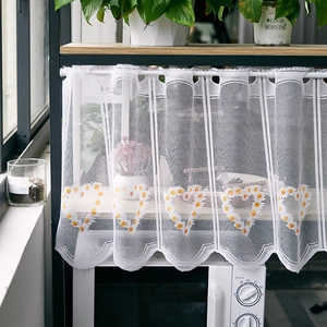 Detailed close-up of white lace curtain featuring yellow daisy embroidery and wavy hem