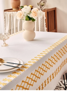 Detail of white rectangular tablecloth with yellow geometric embroidery and floral decor
