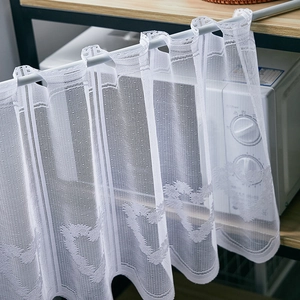 Close-up of white lace kitchen curtain with heart-shaped jacquard and wavy edges