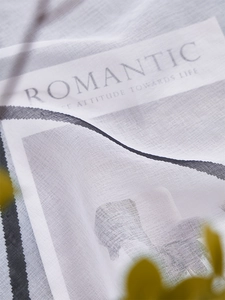 Detail of sheer white lattice fabric with Romantic text print and black striped edges