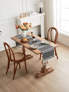 Detail of woven geometric table runner with cotton tassels on dark wood table