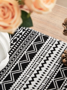 Detailed close-up of monochrome geometric woven table runner with boho fringe on wood