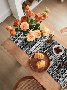 Close-up of black and white geometric woven table runner with boho tassels on wood table