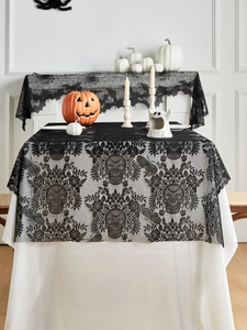 Detail of black lace Halloween table runner featuring skulls on white table with pumpkins