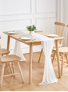 Detail of elegant white chiffon table runner with decorative tied ends on wooden table