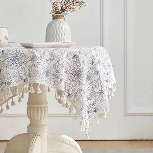 Detail of floral linen tablecloth featuring blue daisy prints and delicate fringe edges