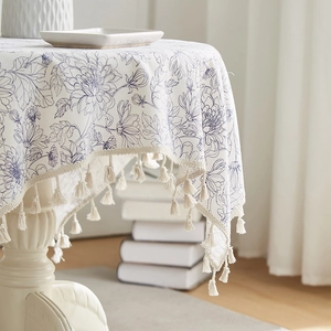 Floral cotton linen tablecloth with blue pattern and elegant fringe tassels on a table