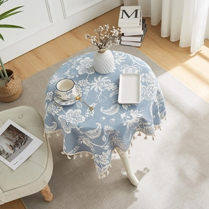 Round blue floral cotton linen tablecloth with beige tassels on a wooden table