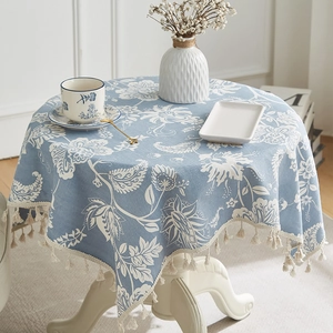 Linen cotton tablecloth with white floral pattern and beige tassels on a round table