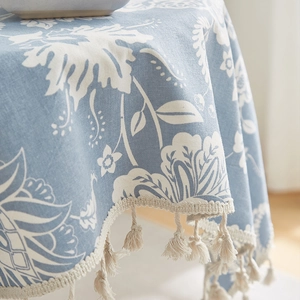 Detail of light blue cotton linen tablecloth with white floral patterns and tassel edges