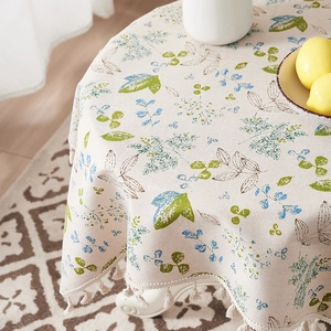 Detail of cotton linen round tablecloth with green leaves pattern and cream tassels