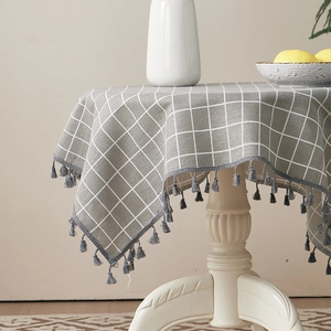 Detail of grey checkered cotton linen tablecloth with delicate grey fringe on round table