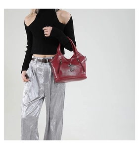 Detail view of red leather tote bag with metal cross decor held by a model