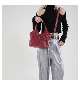 Detail of burgundy glossy leather handbag with cross metal ornament and punk style zippers