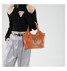 Detail of caramel pebbled leather tote bag with silver cross pendant and side zippers