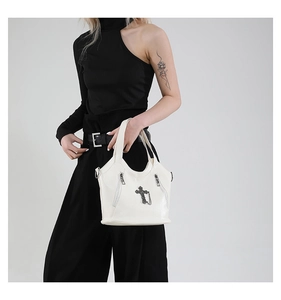 Close-up of white leather tote bag with silver cross pendant and dual zipper detail