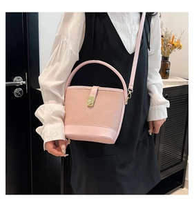 Détail du sac seau rose tressé avec garniture en cuir et boucle en métal doré sur modèle
