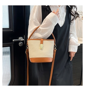 Detail of a contrast bucket bag with straw texture, leather trim and gold twist lock