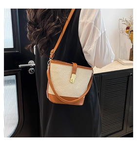 Detail of woven straw bucket bag with brown leather trim and golden twist lock